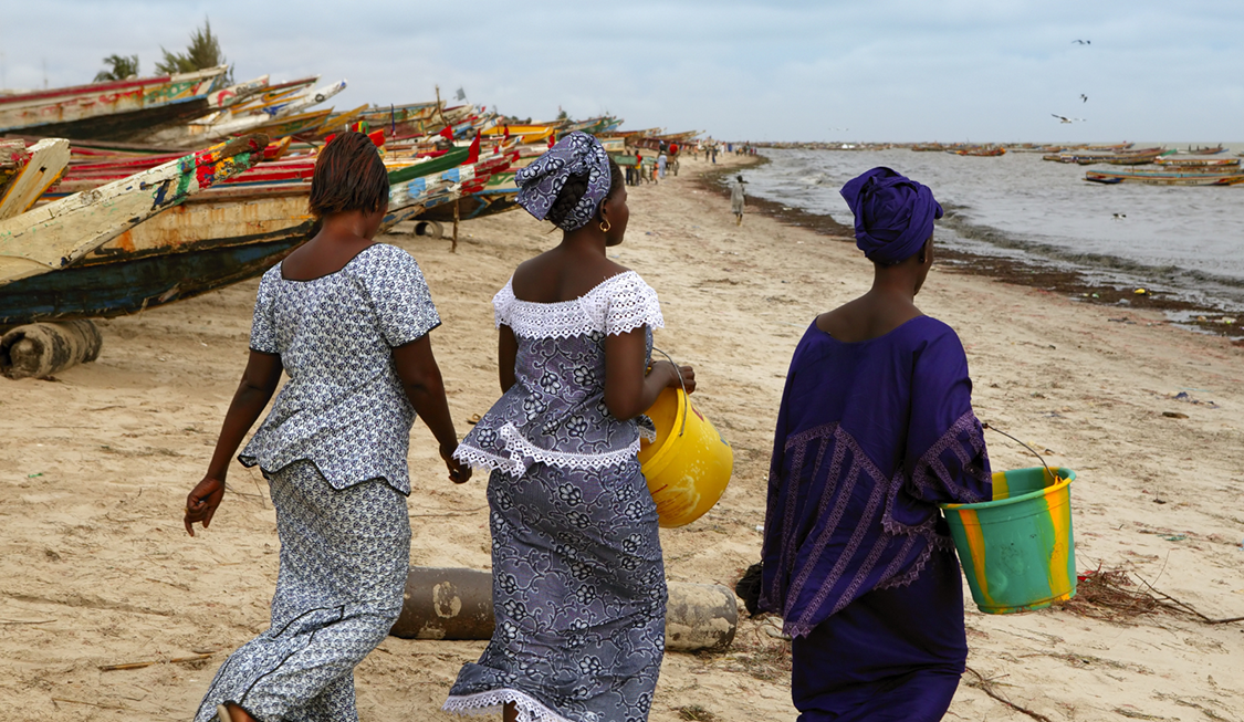 Women in front of fishing boats on a beach in Senegal.